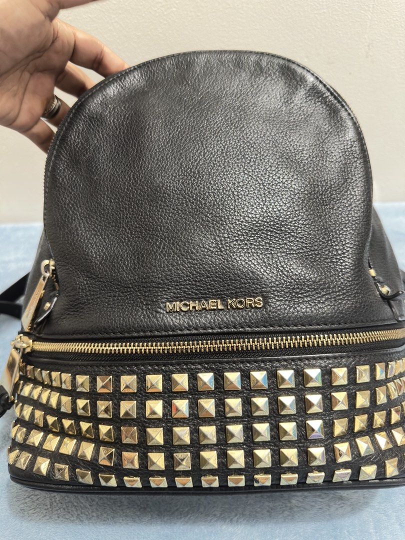 Michael Kors Black Leather Studded Backpack (Category: Backpacks) located in Calamba. Submitted by nympha0630 (Listing ID 1467874137, Image 2). Description: - Brand: Michael Kors - Material: Premium black pebbled leather - Hardware: Gold-tone with engraved zipper pulls & trendy pyramid studs on the front - Compartments: Secure zip-around closure and front zippered pocket - Straps: Adjustable black leather shoulder straps + top handle - Condition: