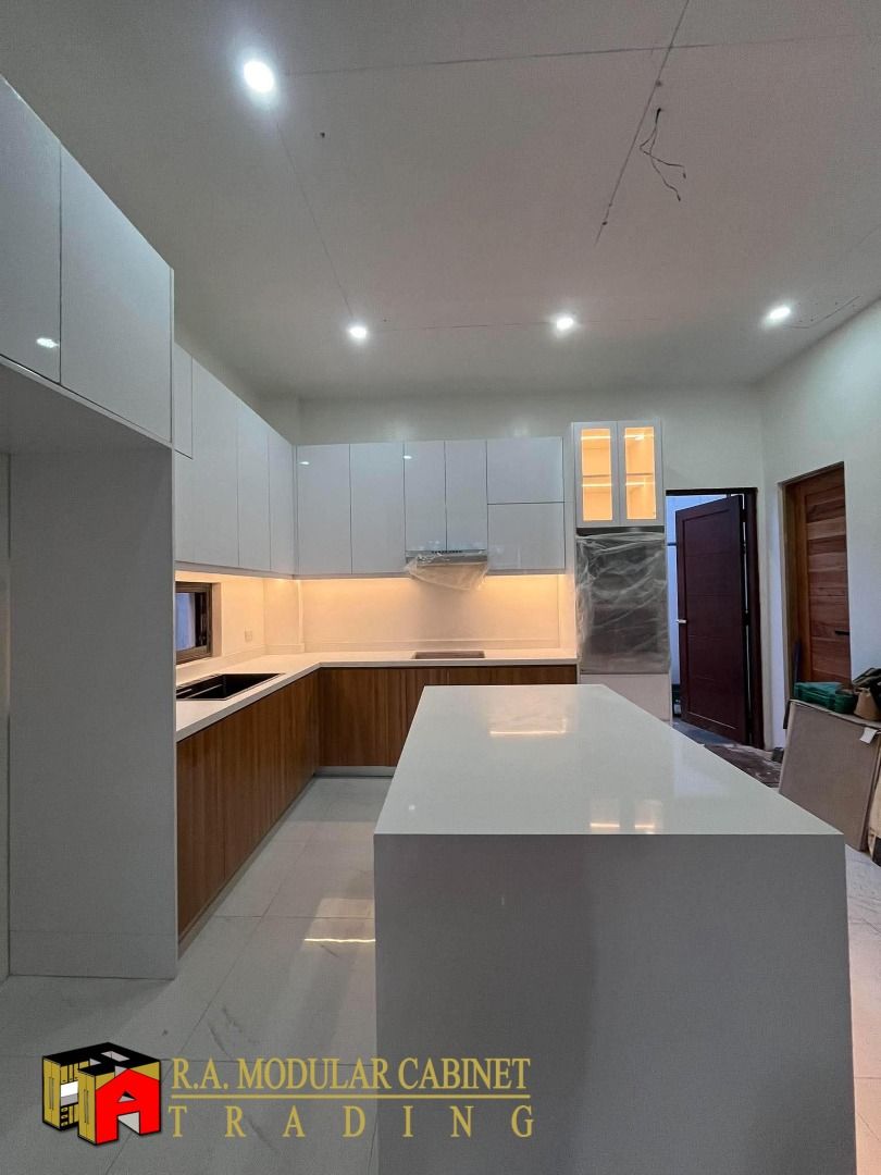 Modern Modular Kitchen Cabinet Set with Island (Category: Shelves, Cabinets & Racks) located in Quezon City. Submitted by ramodularcabinet (Listing ID 1467962441, Image 2). Description: Custom modular kitchen setup by R.A. Modular Cabinet Trading. Glossy white upper cabinets paired with wood grain lower cabinets and white quartz countertops. Includes a large central kitchen island featuring vertical wood slat paneling with built-in warm lighting.