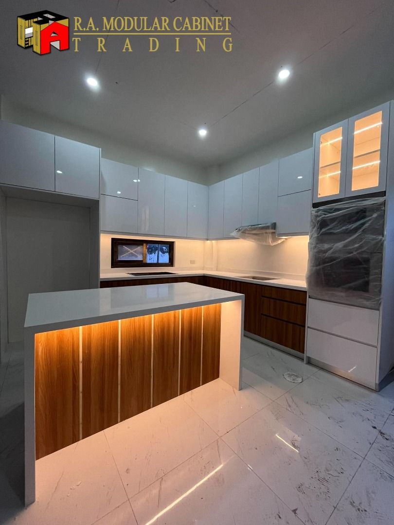 Modern Modular Kitchen Cabinet Set with Island (Category: Shelves, Cabinets & Racks) located in Quezon City. Submitted by ramodularcabinet (Listing ID 1467962441, Image 3). Description: Custom modular kitchen setup by R.A. Modular Cabinet Trading. Glossy white upper cabinets paired with wood grain lower cabinets and white quartz countertops. Includes a large central kitchen island featuring vertical wood slat paneling with built-in warm lighting.