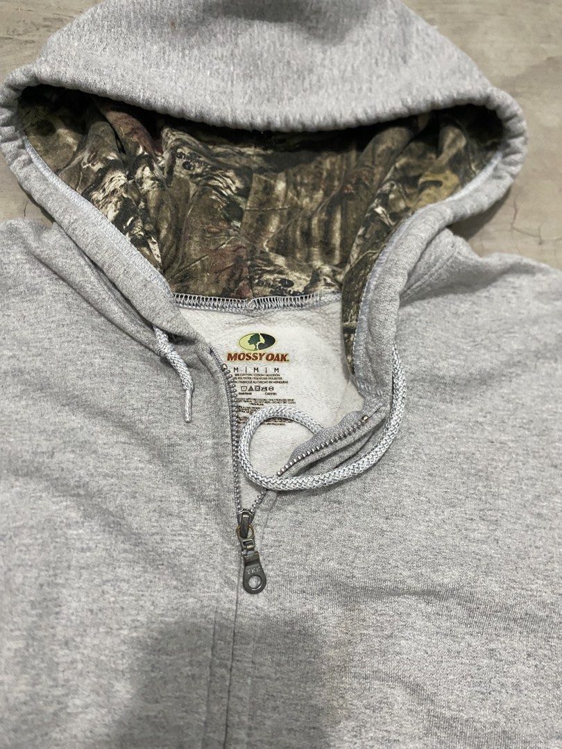 Mossy Oak Camo Lined Grey Zip Realtree (Category: Coats, Jackets and Outerwear) located in Las Pinas. Submitted by 2fly.margiela (Listing ID 1467870546, Image 2). Description: - Brand: Mossy Oak - Size: Medium - Color: Grey with camo-lined hood - Material: Cotton blend - Features: Full zip-up closure, drawstring hood, and front kangaroo pockets - Fit: Standard fit, perfect for casual wear and cooler days - Condition: Excellent.