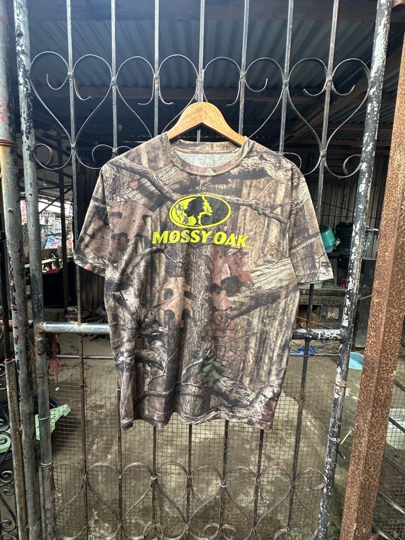 Mossy Oak Camo T-Shirt Break-Up Pattern (Category: Tshirts & Polo Shirts ) located in Lapu Lapu. Submitted by gabocamaon03138 (Listing ID 1468024700, Image 1). Description: - Brand: Mossy Oak - Design: Classic tree branch and leaf camo print - Detail: Bright yellow chest logo with vintage cracking - Style: Short sleeves, crew neck - Material: Soft, broken-in cotton blend - Condition: Great pre-loved condition, super comfortable - Perfect for outd