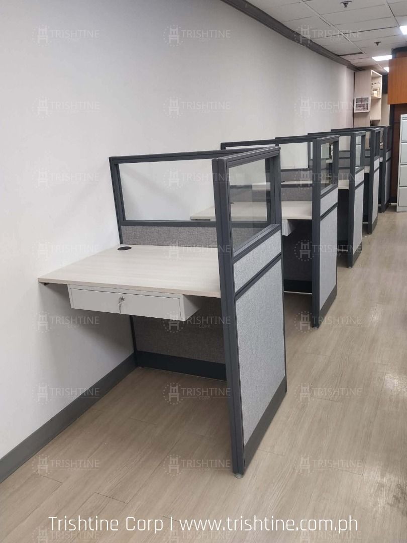 Office Workstation Cubicle Partition Desk (Category: Office Furniture & Fixtures) located in Caloocan City. Submitted by jim.trishtineofficefurnitures (Listing ID 1467887872, Image 3). Description: - Modular office cubicle designed for call centers and open layouts - Stylish grey fabric panels with modern glass top dividers - Durable light wood grain desktop featuring a convenient pull-out drawer - Built-in cable management grommet hole to keep w
