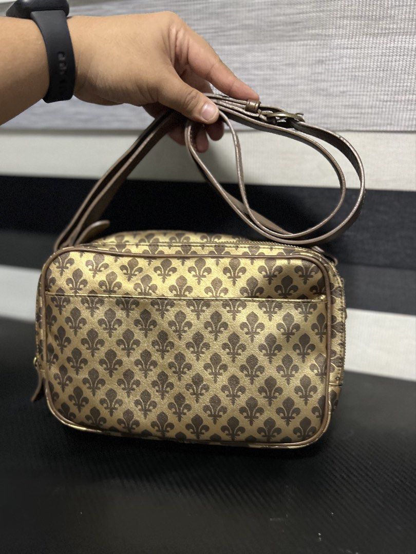 Patrick Cox Monogram Crossbody Bag Gold Brown (Category: Luxury Bags & Wallets) located in Calasiao. Submitted by pb.supply_v2 (Listing ID 1468050840, Image 2). Description: Patrick Cox crossbody bag in gold and brown tones. All-over fleur-de-lis monogram pattern printed on the exterior. Dual zip compartments up top with a brown lining inside. Includes an adjustable strap and an interior slip pocket with the brand label stitched inside. Clean str