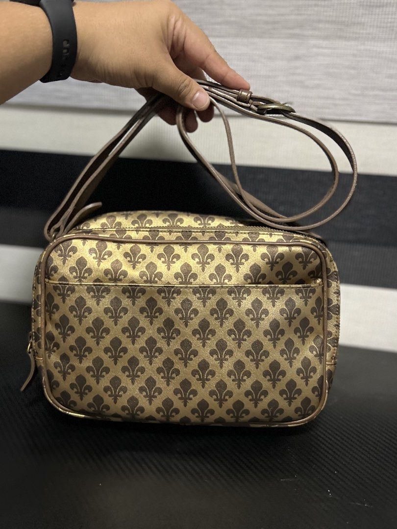 Patrick Cox Monogram Crossbody Bag Gold Brown (Category: Luxury Bags & Wallets) located in Calasiao. Submitted by pb.supply_v2 (Listing ID 1468050840, Image 1). Description: Patrick Cox crossbody bag in gold and brown tones. All-over fleur-de-lis monogram pattern printed on the exterior. Dual zip compartments up top with a brown lining inside. Includes an adjustable strap and an interior slip pocket with the brand label stitched inside. Clean str
