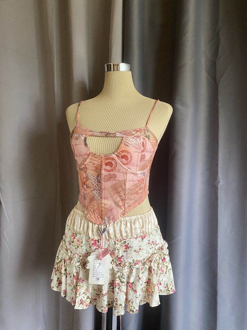 Outcast Pink Vintage Postcard Keyhole Corset Top (Category: Sleeveless) located in Cagayan de Oro. Submitted by curated_closetph (Listing ID 1467937897, Image 2). Description: — Size : M - L — Color: Pink / Peach — Vintage postcard and stamp print for a retro aesthetic — Upper bust keyhole cutout detail — Underwire cups for support and shaping — Adjustable spaghetti straps with delicate lace trim — Lace-up ribbon back with metal grommets — Pointe