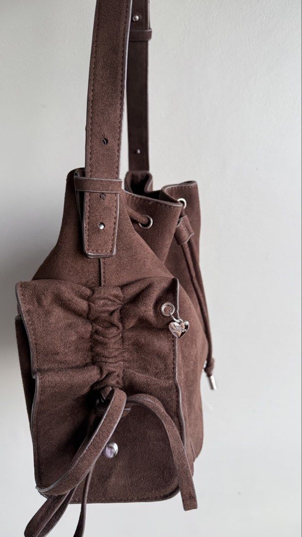 Pony Twenty Eight Suede Bucket Bag (Category: Shoulder Bags) located in Pasay City. Submitted by maviemavz (Listing ID 1467893397, Image 2). Description: - Material: Brown suede with brown fabric interior lining - Closure: Secure drawstring top with silver hardware - Exterior: Side pockets accented with cute tiny heart charms - Strap: Adjustable shoulder strap for a custom fit - Interior: Includes a zipper pocket and slip pockets for organization