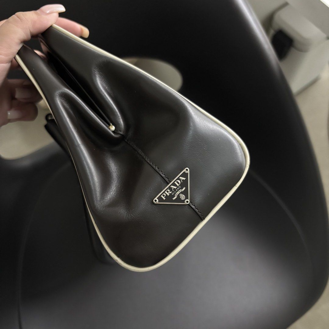 Prada Vitello Frame Kiss-Lock Handbag (Category: Luxury Bags & Wallets) located in Makati City. Submitted by dianedelro (Listing ID 1467941092, Image 2). Description: - Authentic Prada brown leather handbag with striking contrast white piping - Features a wide-opening frame closure and sturdy double top handles with buckle details - Iconic Prada metal triangle logo badge on the exterior - Luxurious olive green fabric interior featuring the repeat