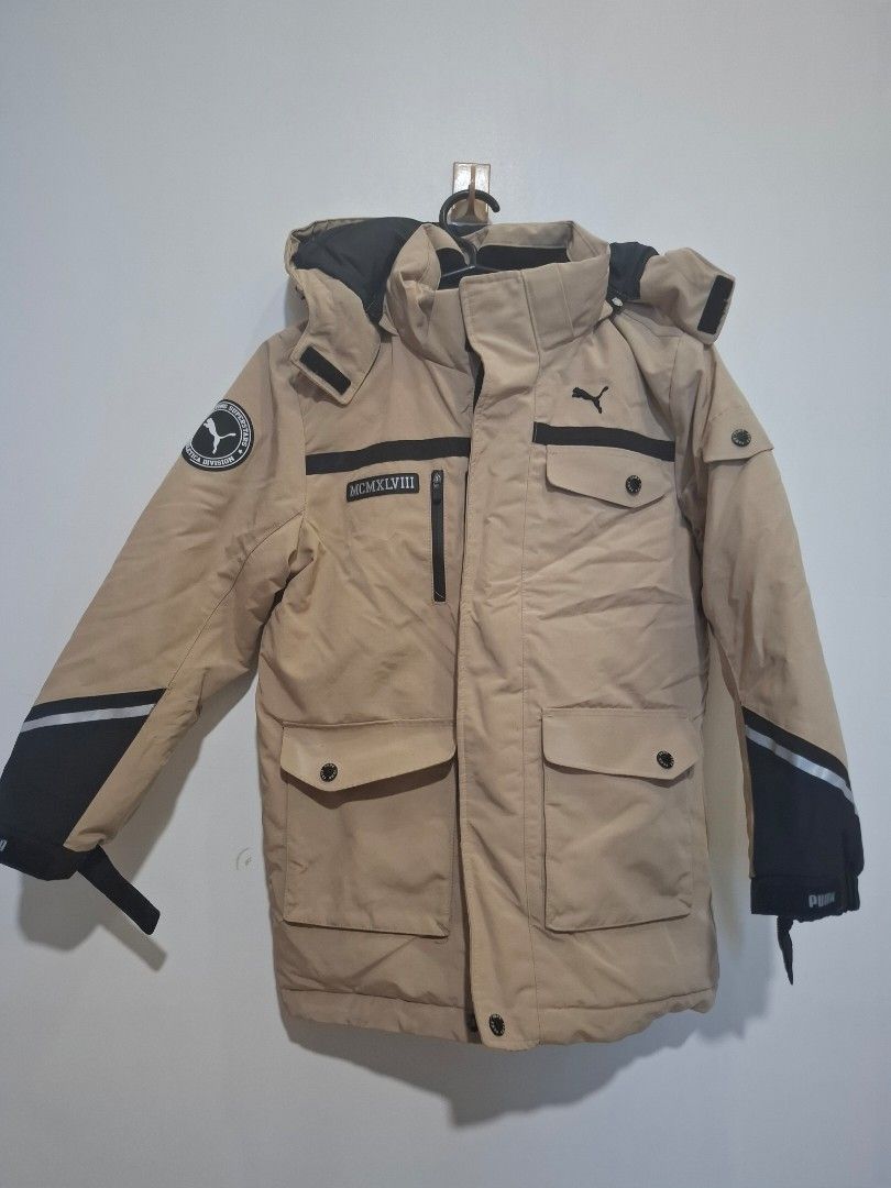 Puma Winter Jacket Beige Black Hooded Coat (Category: Babies & Kids Fashion) located in Imus. Submitted by maggieforce (Listing ID 1467922382, Image 2). Description: - size 120 on tag - Brand: Puma - Color: Tan with black contrast panels - Features: Hooded, thick padded lining for cold and snowy weather - Closure: Zip front with button flap - Pockets: Multiple functional pockets on chest and lower front - Details: Roman numerals graphic and Puma 