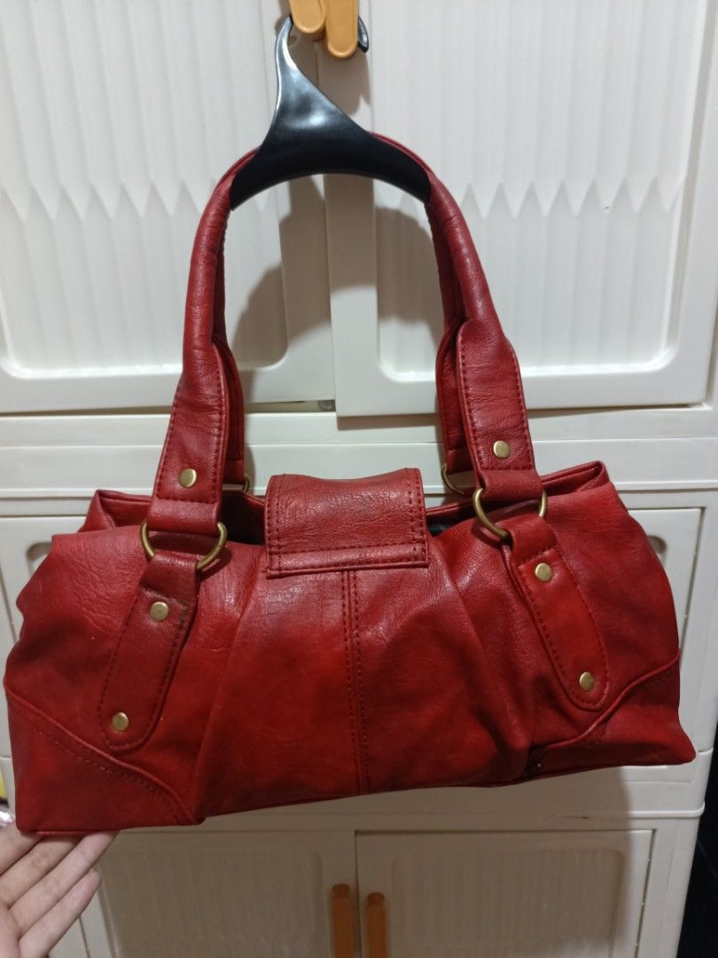 Red leather shoulder handbag with gold hardware (Category: Luxury Bags & Wallets) located in Manila. Submitted by del_thrifts03 (Listing ID 1467986784, Image 2). Description: - Color & Material: Red textured faux leather with dark fabric lining - Closure: Secure metal turn-lock on the front flap - Handles: Dual red handles with brass-toned rings and decorative studs - Interior: Roomy storage space with a built-in zipper compartment and side pocke