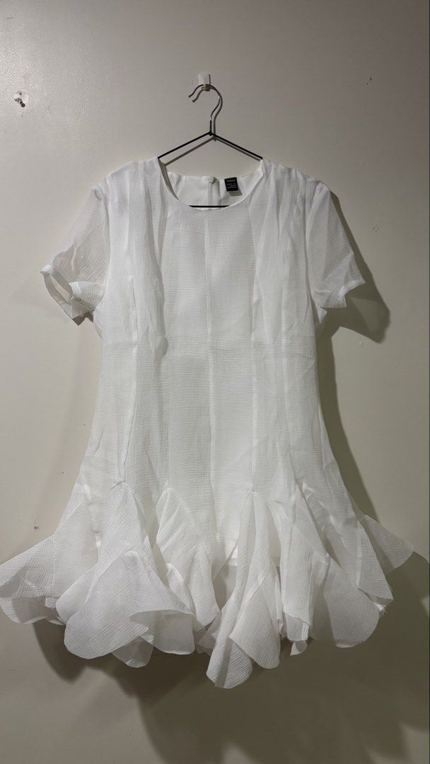 Shein Ruffled White Mini Dress (Category: Dresses) located in Binan City. Submitted by myprelovedhaul (Listing ID 1467948195, Image 2). Description: This item is a white crewneck short-sleeve mini dress featuring a distinctive dramatic layered ruffle hem. It is made from a lightweight, subtly textured semi-sheer fabric with panel detailing down the front torso that creates a structured, tailored look before flaring out into voluminous, cascading 
