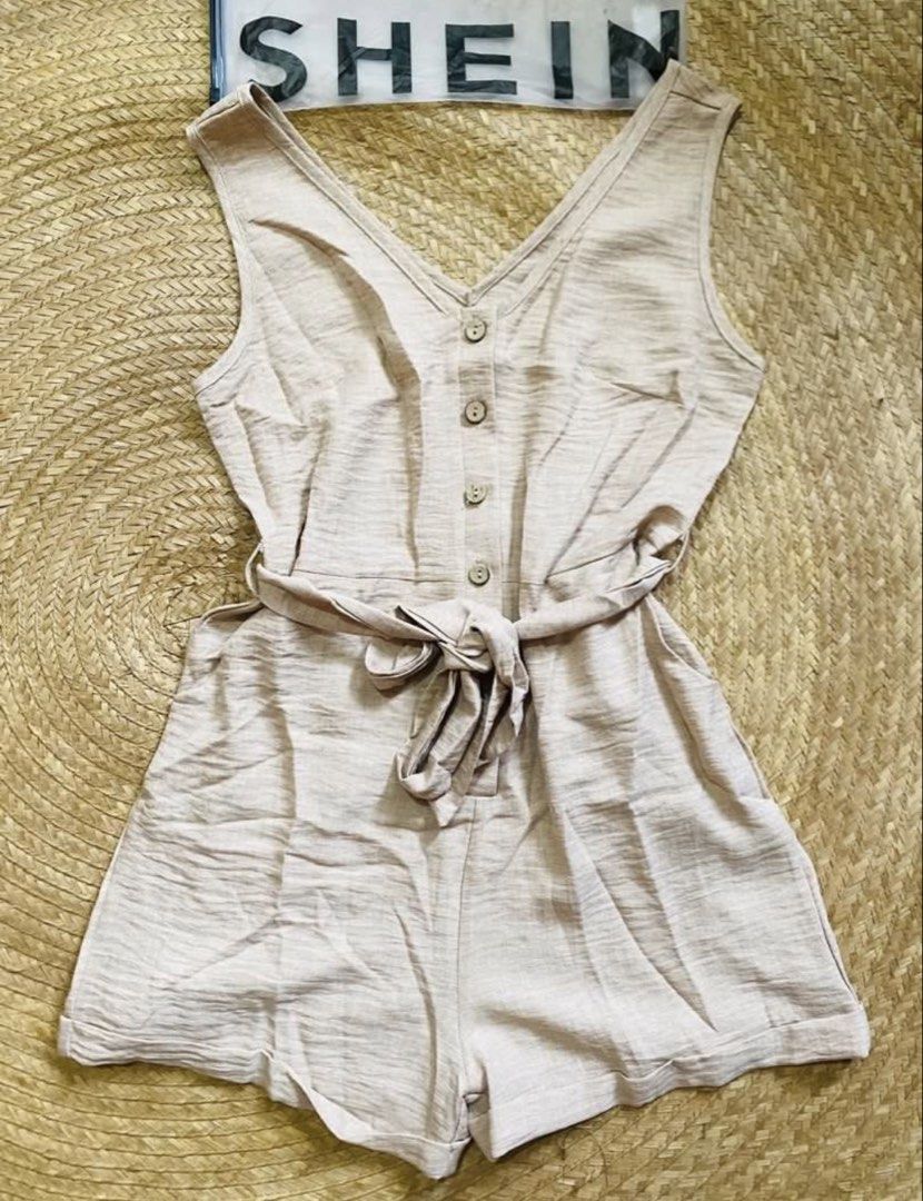 SHEIN V-Neck Button Front Belted Romper (Category: Rompers) located in Marikina City. Submitted by jessylady10 (Listing ID 1467982190, Image 1). Description: - Brand: SHEIN - Color: Classic Beige - Material: Textured cotton-linen blend (lightweight and breathable) - Design: Sleeveless, V-neckline, front button placket with brown buttons - Fit: Includes a matching tie belt to cinch the waist and trendy rolled hem shorts - Condition: Brand new with