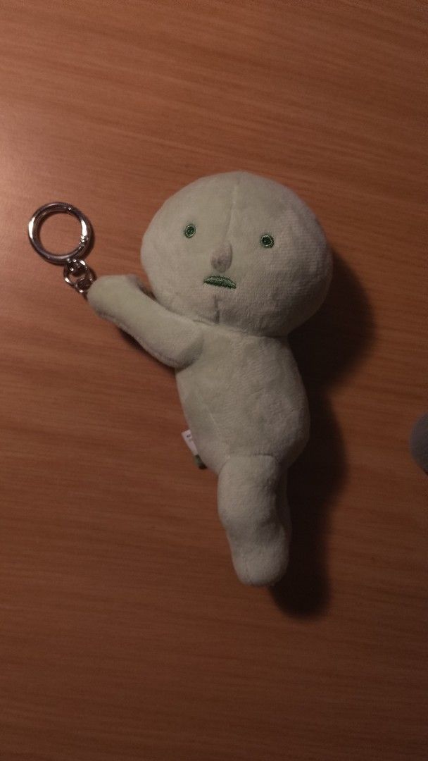 Smiski Plush Keychain (Category: Plushies & Soft Toys) located in Mandaluyong City. Submitted by dennisells (Listing ID 1467856174, Image 1). Description: - Official Smiski plush keychain in pale green - Soft fabric texture with cute embroidered face details - Features an attached metal keyring for easy attachment to bags or keys - Includes green tag with Smiski in Japanese and English katakana - Condition: Clean surface with tag intact.