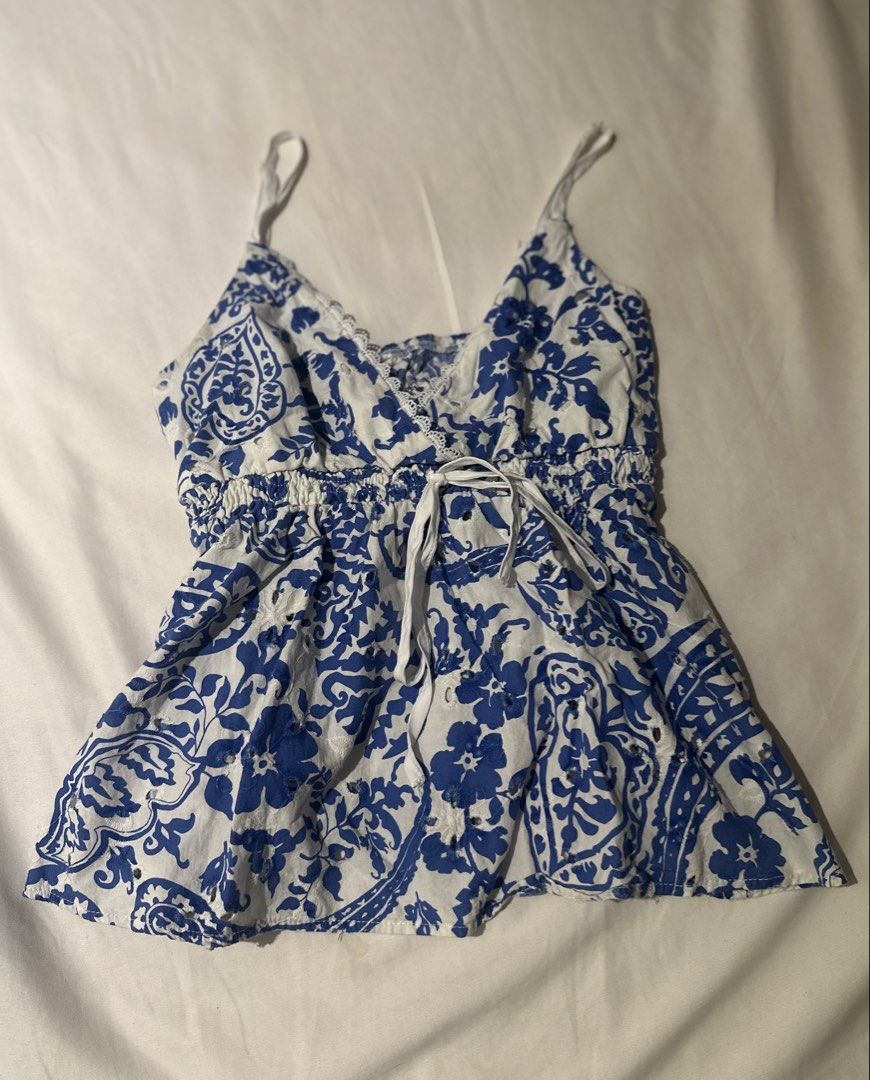summer blue white toile patterned floral cami top (Category: Sleeveless) located in Quezon City. Submitted by kalmai (Listing ID 1467930294, Image 1). Description: - Color & Pattern: Blue and white floral - Neckline: V-neck with delicate lace trim - Waist: Smocked elastic with functional front drawstring tie - Straps: Adjustable/light spaghetti straps - Details: Eyelet cutout patterns and a soft peplum hem - Condition/Vibe: Great breezy piece for