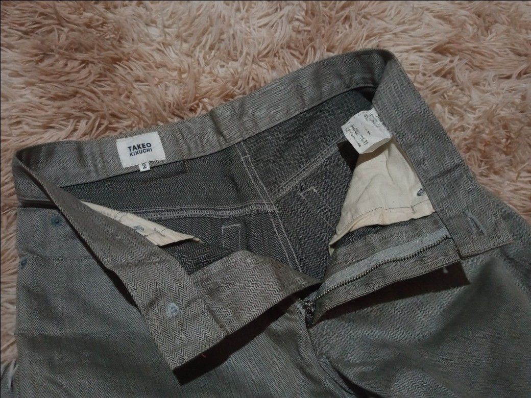 Takeo Kikuchi Herringbone Pattern Pants Size 2 (Category: Jeans) located in Boston. Submitted by johnpaulvi30029 (Listing ID 1467999151, Image 3). Description: Takeo Kikuchi gray trousers with a distinct herringbone weave pattern throughout. Size 2 on the inner waist label. Button fly closure, front pockets, and rear patch pockets. Straight leg cut. Clean interior lining with Japanese care tags. Neutral tone works easily with various tops..