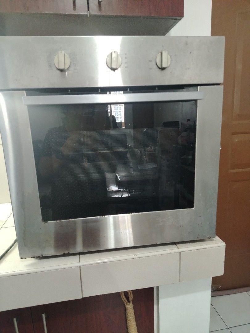 Tekno Built-in Oven Stainless Steel (Category: Ovens & Toasters) located in Makati City. Submitted by mercianalech (Listing ID 1468059054, Image 2). Description: - Type: Stainless steel built-in kitchen oven - Controls: Three knobs on the top panel - Door: Drop-down glass door - Interior: Includes racks, metal baking trays, and a back wall fan vent - Condition: Outer metal housing shows wear, water marks, and minor rust along the edges.