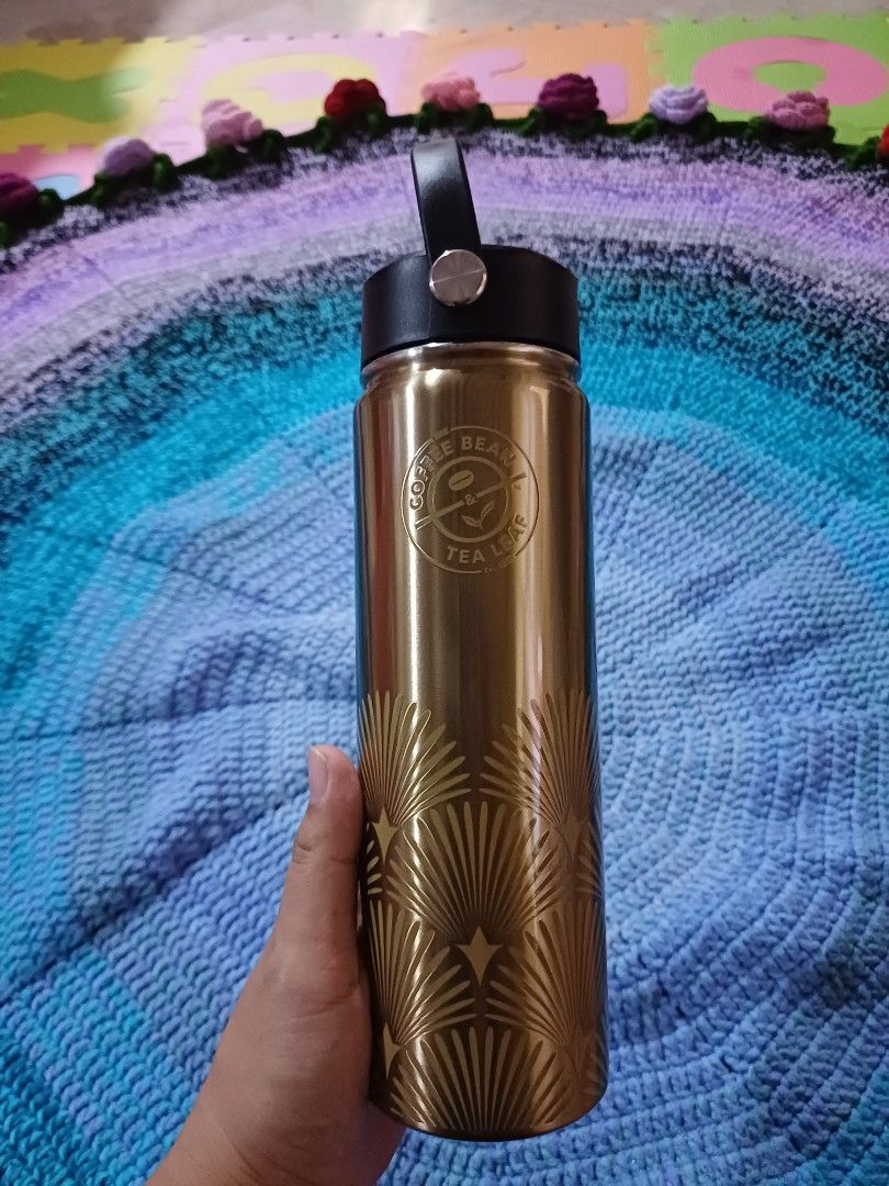 The Coffee Bean & Tea Leaf CBTL Gold Water Bottle (Category: Water Bottles & Tumblers) located in San Pedro. Submitted by purpledream0316 (Listing ID 1467907955, Image 1). Description: - Brand: The Coffee Bean & Tea Leaf - Color/Design: Gold with a stylish geometric fan pattern - Cap: Black screw-on cap with a convenient built-in carry handle - Performance: Keeps beverages hot or cold while on the go - Compatibility: Fits nicely in standard cup h