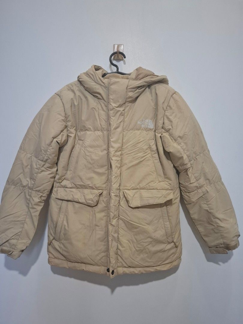 The North Face Puffer Jacket Beige (Category: Babies & Kids Fashion) located in Imus. Submitted by maggieforce (Listing ID 1467915545, Image 1). Description: - size 140 on tag - Brand: The North Face - Color: Neutral beige / Earth tone - Features: Attached hood, zip-up front closure with button flap, and quilted design - Pockets: Multiple front pockets with flaps for secure storage - Branding: White embroidered logo on the chest and back shoulder