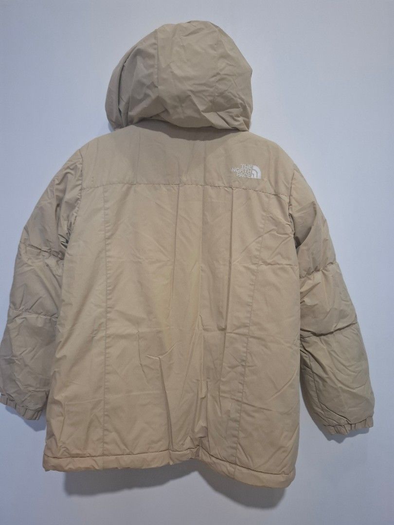 The North Face Puffer Jacket Beige (Category: Babies & Kids Fashion) located in Imus. Submitted by maggieforce (Listing ID 1467915545, Image 2). Description: - size 140 on tag - Brand: The North Face - Color: Neutral beige / Earth tone - Features: Attached hood, zip-up front closure with button flap, and quilted design - Pockets: Multiple front pockets with flaps for secure storage - Branding: White embroidered logo on the chest and back shoulder