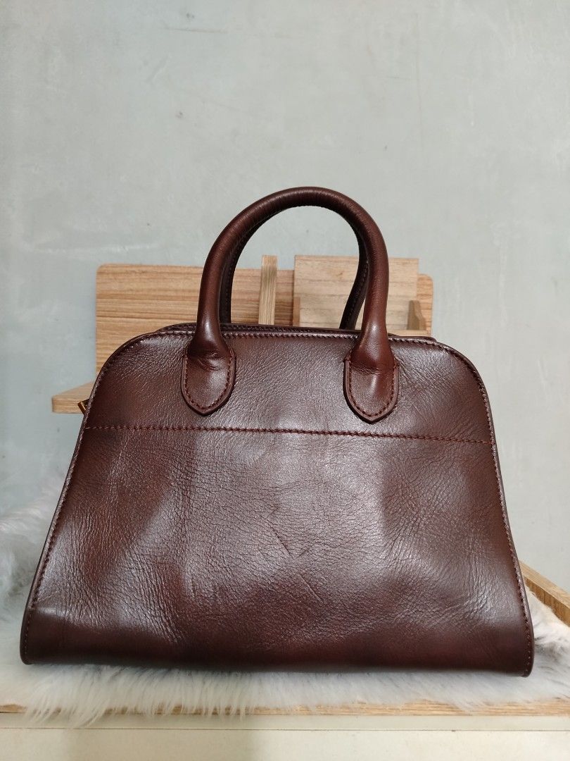 The Row Margaux 10 (Category: Tote Bags) located in Lucena. Submitted by gracious_chin0436 (Listing ID 1467841349, Image 2). Description: - Brand: The Row - Color: Rich brown - Material: Premium pebbled leather with clean stitching - Hardware: Gold-tone side buckle and logo stamp - Design: Structured shape with dual top handles - Protection: Four metal feet on the bottom base - Handbag only missing long strap for crossbody -with normal to minimal