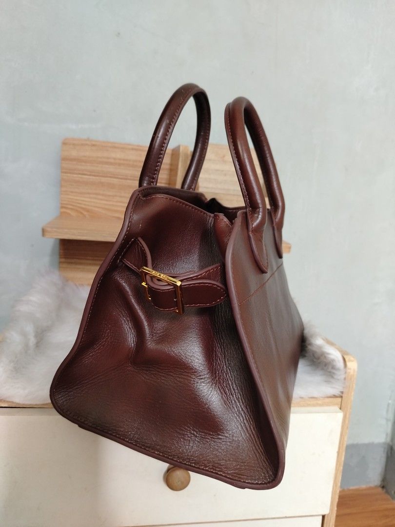 The Row Margaux 10 (Category: Tote Bags) located in Lucena. Submitted by gracious_chin0436 (Listing ID 1467841349, Image 3). Description: - Brand: The Row - Color: Rich brown - Material: Premium pebbled leather with clean stitching - Hardware: Gold-tone side buckle and logo stamp - Design: Structured shape with dual top handles - Protection: Four metal feet on the bottom base - Handbag only missing long strap for crossbody -with normal to minimal