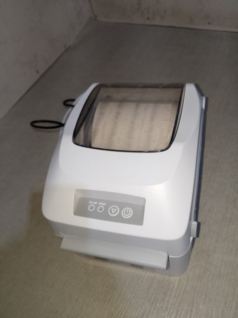 Thermal Label Printer (Category: Printers, Scanners & Copiers) located in Baliuag. Submitted by daisy0215 (Listing ID 1467967656, Image 1). Description: - Sleek white desktop label printer with a space-saving compact footprint - Clear top window lets you easily monitor remaining paper roll - Convenient front control buttons for power and feed - Comes complete with power cable and handy QR code stickers near the bottom edge - Ideal for home office
