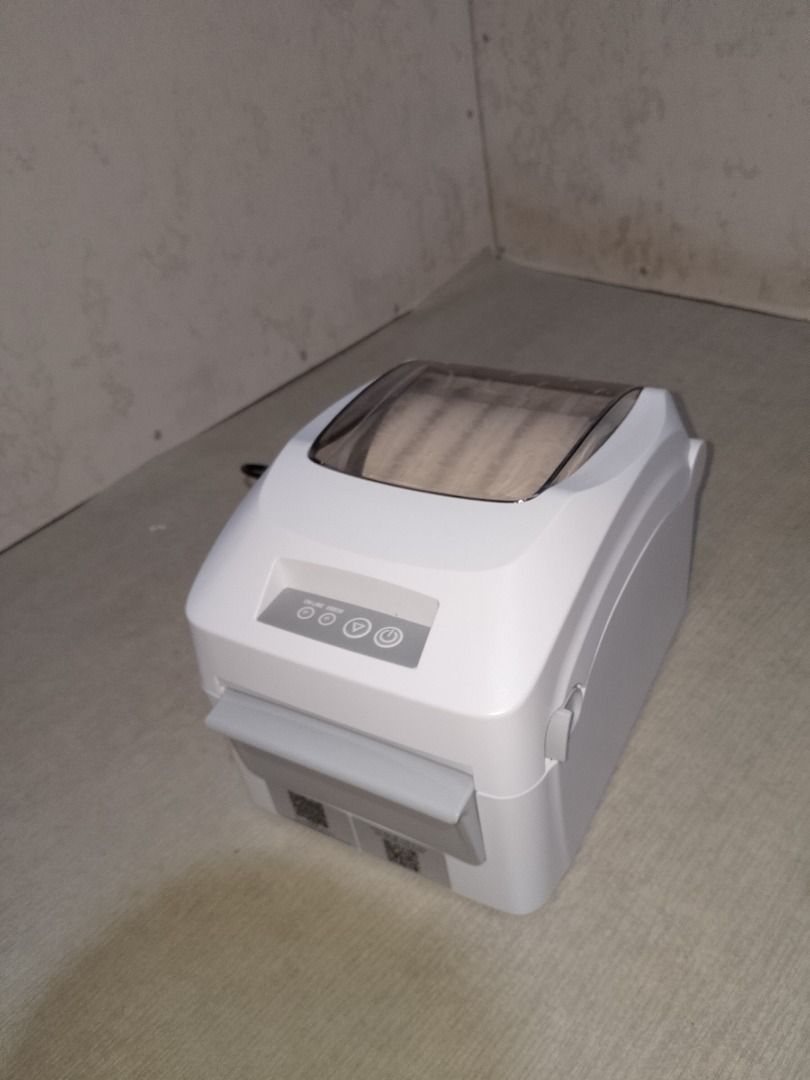 Thermal Label Printer (Category: Printers, Scanners & Copiers) located in Baliuag. Submitted by daisy0215 (Listing ID 1467967656, Image 3). Description: - Sleek white desktop label printer with a space-saving compact footprint - Clear top window lets you easily monitor remaining paper roll - Convenient front control buttons for power and feed - Comes complete with power cable and handy QR code stickers near the bottom edge - Ideal for home office