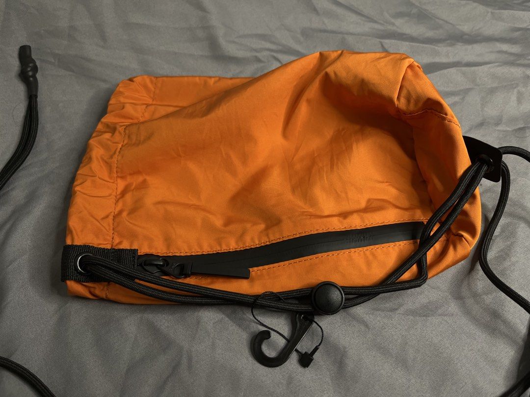 Uniqlo Orange Drawstring Crossbody Bag (Category: Cross-body Bags) located in Imus. Submitted by graeyowl (Listing ID 1467984905, Image 2). Description: Bright orange crossbody bag made from 100% polyester. Features a black zippered front pocket with YKK hardware, adjustable black drawstring cord, and a small attached hook. Grey interior lining. Clean tag inside showing material breakdown and made in China details. Lightweight utility style, easy
