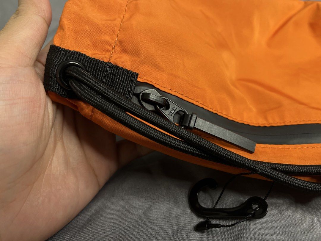 Uniqlo Orange Drawstring Crossbody Bag (Category: Cross-body Bags) located in Imus. Submitted by graeyowl (Listing ID 1467984905, Image 3). Description: Bright orange crossbody bag made from 100% polyester. Features a black zippered front pocket with YKK hardware, adjustable black drawstring cord, and a small attached hook. Grey interior lining. Clean tag inside showing material breakdown and made in China details. Lightweight utility style, easy