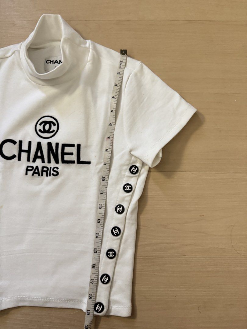 Vintage Chanel Top (Category: Shirts) located in Manila. Submitted by juhjuh (Listing ID 1467914046, Image 3). Description: - Authentic Chanel short sleeve top in crisp white S/M - Chic mock neckline with branded inner neck label - Bold black 'Chanel Paris' logo and CC symbol on the chest - Unique decorative black and white CC buttons along both side seams - Flattering, fitted cut with a clean fabric finish - Condition: Excellent / Like new.