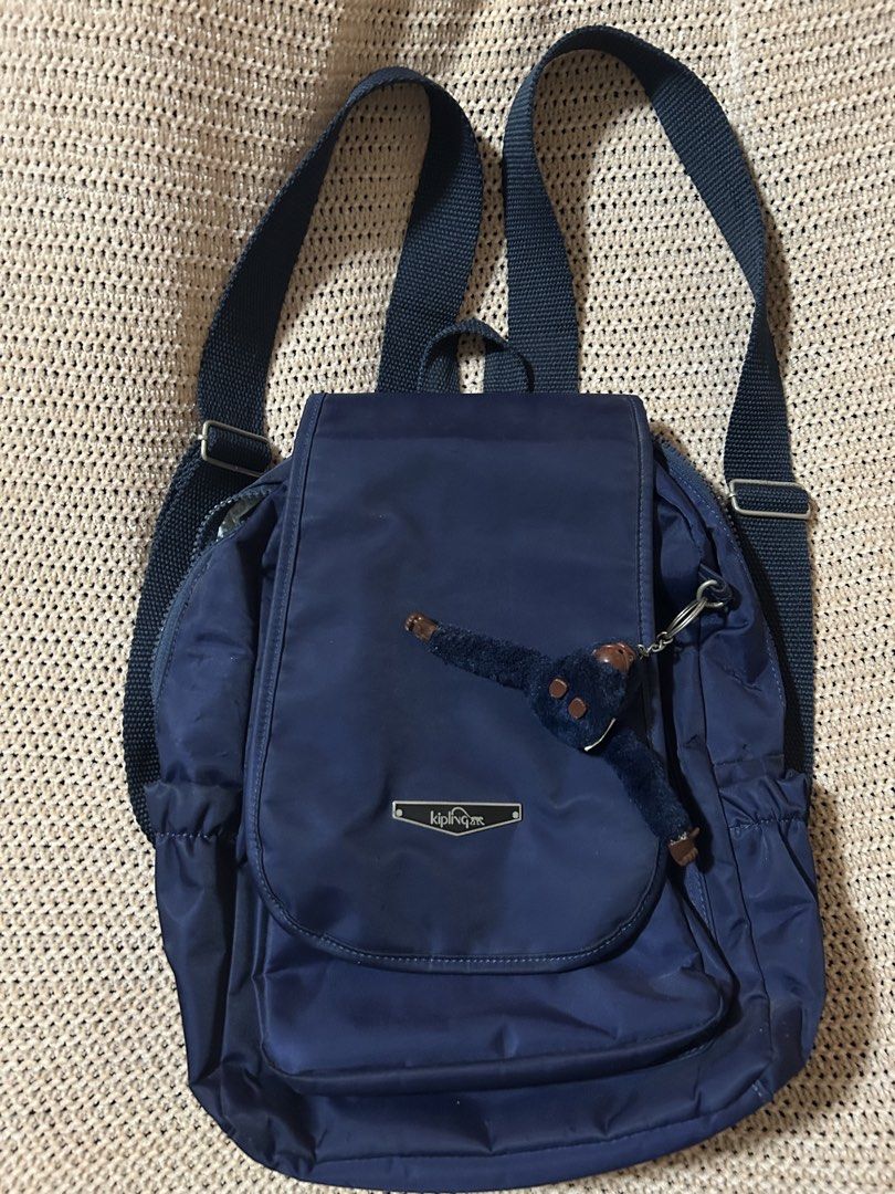 Vintage Kipling Navy Blue Backpack with Monkey Keychain (Category: Backpacks) located in Pasig City. Submitted by mixpicks (Listing ID 1467857509, Image 1). Description: - Color: Dark Blue - Material: Lightweight, durable nylon - Closure: main compartment with secure flap cover - Pockets: Front zippered pocket with snap flap cover and convenient side pockets - Comfort: Adjustable shoulder straps for a custom fit - Inclusion: Comes with the iconic