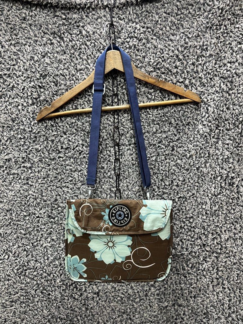 vintage Y2K-era Kipling crossbody bag (Category: Cross-body Bags) located in General Trias. Submitted by zrchustle.604 (Listing ID 1468055403, Image 1). Description: vintage Y2K-era Kipling crossbody bag featuring a distinctive brown nylon base printed with turquoise-blue and white hibiscus floral motifs and whimsical swirls. It is fitted with an adjustable blue webbing shoulder strap and prominently displays the signature round rubberized Kiplin