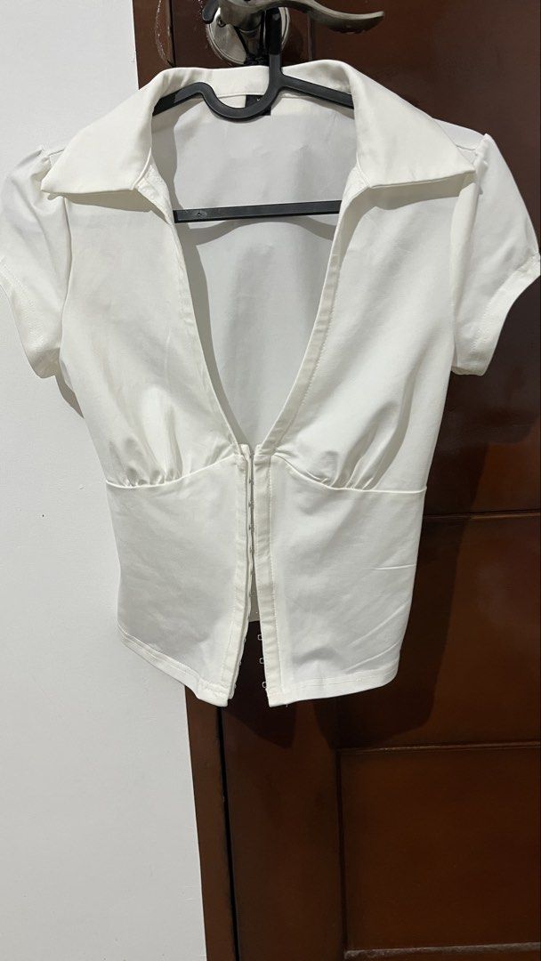 White Short Sleeve Collared Crop Top with Hook and Eye Front (Category: Shirts) located in Cebu City. Submitted by minymal (Listing ID 1468010882, Image 2). Description: - Color: White - Size: XS (Made in China) - Style: Cropped, fitted body with short sleeves - Details: Collar neckline, deep V-neck, metal hook-and-eye front closures - Condition: Clean, no stains or damage, ready to wear.