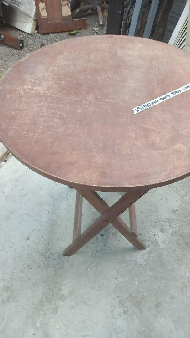 Wooden Round Folding Table (Category: Tables & Sets) located in Quezon City. Submitted by madelrivera (Listing ID 1468005351, Image 1). Description: - Type: Round wooden table with crossed folding legs - Finish: Brown with visible surface wear and scuffs on top - Storage: Folds flat for easy and compact storage - Build: Sturdy construction for reliable everyday use - Best For: Small spaces, balconies, or extra dining seating.