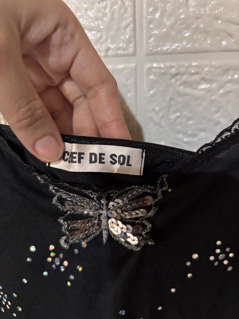 Y2k Goth sequin top (Category: Sleeveless) located in Cebu City. Submitted by airahxoxo (Listing ID 1467915848, Image 2). Description: - Brand: Cef De Sol - Style: Black spaghetti strap cami with Y2K fairy grunge vibe - Details: Shiny iridescent rhinestones on the front and silver sequin butterfly applique at the neckline - Design: V-neck with lace trim and sheer lace ruffle hem - Fabric: Lightweight, comfortable wardrobe staple.