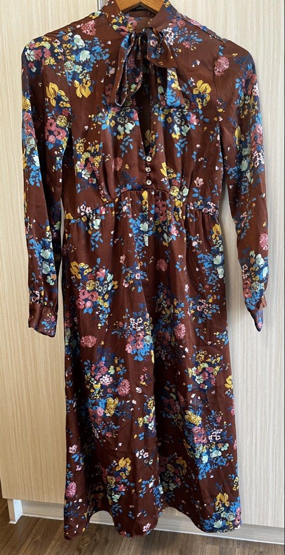 Zara Basic Floral Brown Long Sleeve Dress (Category: Dresses) located in Manila. Submitted by lorenasant37621 (Listing ID 1467900799, Image 1). Description: - Brand: Zara Basic - Style: Midi dress with relaxed skirt and fitted waist - Color/Pattern: Brown with vibrant blue, yellow, and pink floral print - Details: High neckline with self-tie bow ribbon, partial front button placket, long sleeves with buttoned cuffs (1 button missing) - Material: 