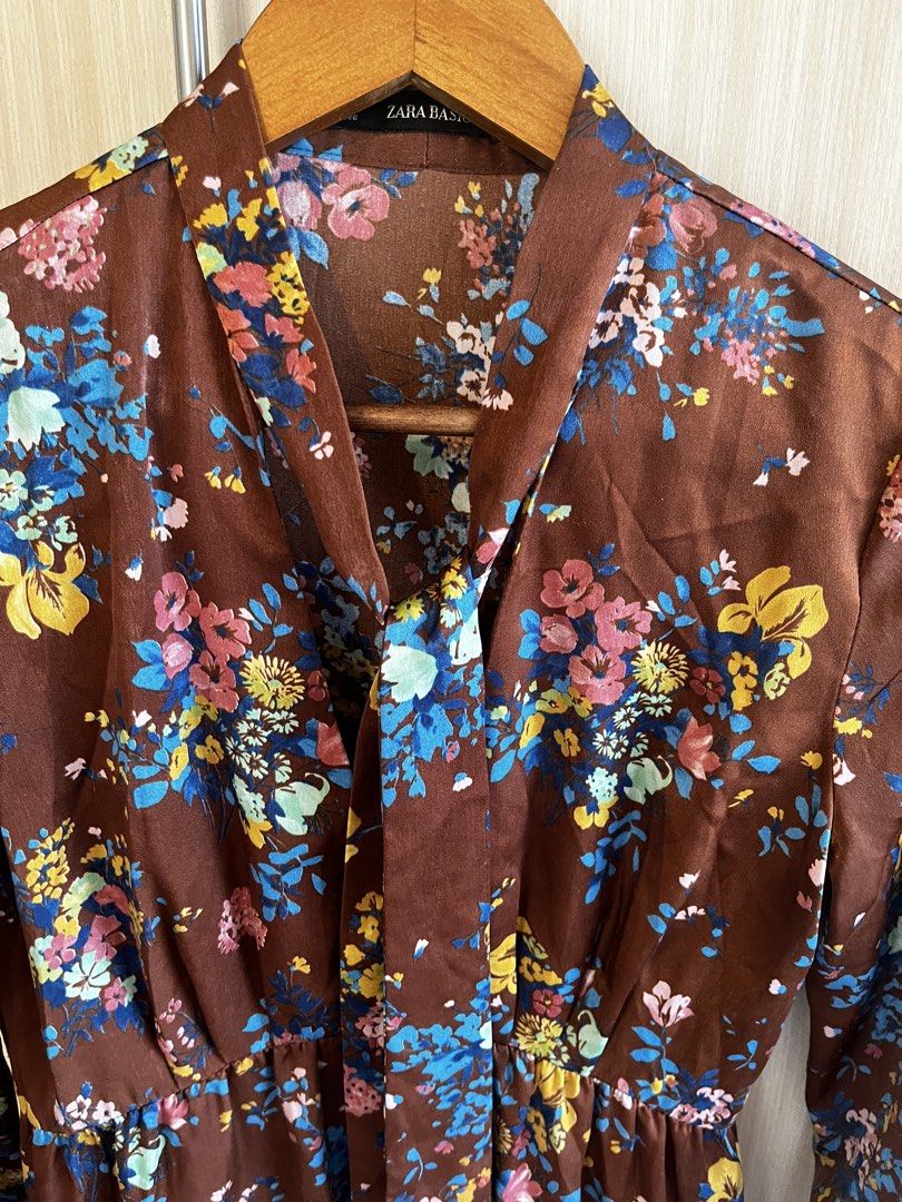 Zara Basic Floral Brown Long Sleeve Dress (Category: Dresses) located in Manila. Submitted by lorenasant37621 (Listing ID 1467900799, Image 2). Description: - Brand: Zara Basic - Style: Midi dress with relaxed skirt and fitted waist - Color/Pattern: Brown with vibrant blue, yellow, and pink floral print - Details: High neckline with self-tie bow ribbon, partial front button placket, long sleeves with buttoned cuffs (1 button missing) - Material: 