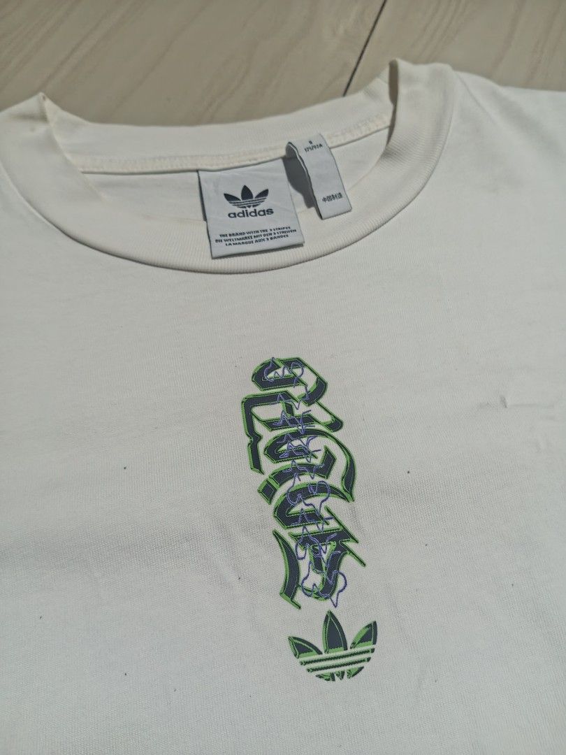 Adidas White Graphic Tee Size S (Category: Tshirts & Polo Shirts ) located in Manila. Submitted by charleshustla (Listing ID 1468195467, Image 2). Description: - Brand: Adidas - Size: Small (S) - Color: Clean White - Design Front: Vertical gothic lettering with iconic trefoil logo - Design Back: Large globe graphic with multilingual text and German Engineering stamp - Fit: Short sleeves, classic crew neck - Condition: Excellent, ready to wear.