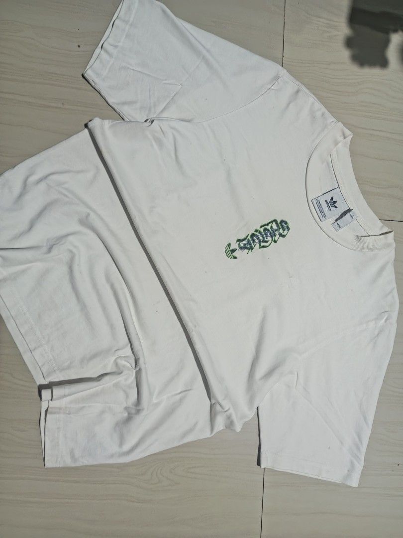 Adidas White Graphic Tee Size S (Category: Tshirts & Polo Shirts ) located in Manila. Submitted by charleshustla (Listing ID 1468195467, Image 1). Description: - Brand: Adidas - Size: Small (S) - Color: Clean White - Design Front: Vertical gothic lettering with iconic trefoil logo - Design Back: Large globe graphic with multilingual text and German Engineering stamp - Fit: Short sleeves, classic crew neck - Condition: Excellent, ready to wear.