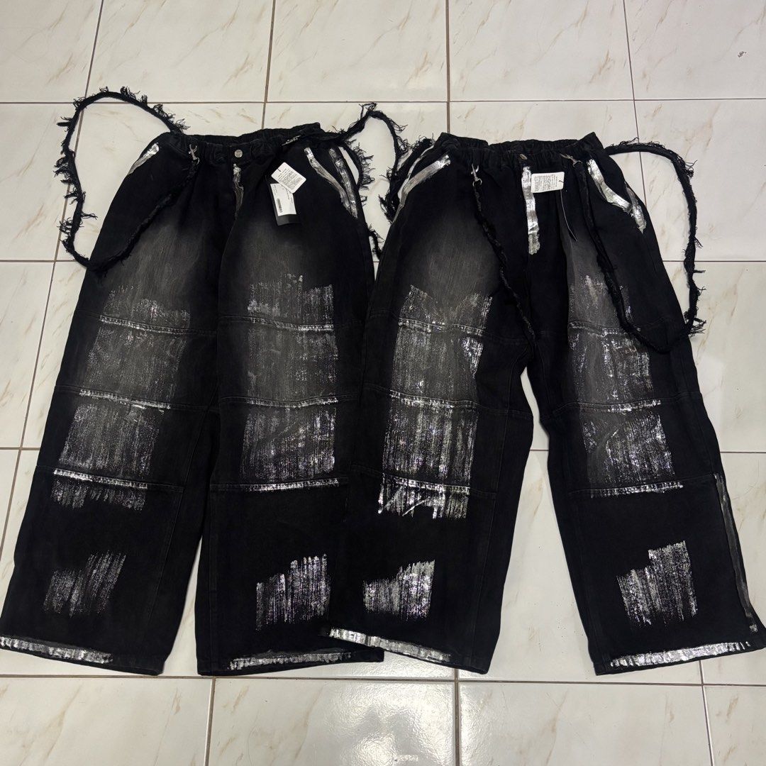 Adrer japanese pants (Category: Jeans) located in San Fernando. Submitted by diff.thr1ft (Listing ID 1468115366, Image 1). Description: - Brand: Adrer - Color: Black with silver metallic/foil distressed print details - Style: Japanese streetwear, wide-leg fit - Features: Elastic high waist, distressed raw edges, side straps with metal hardware, branded button - Condition: Brand new with tags (BNWT) - Perfect for daily casual wear or edgy streetwe