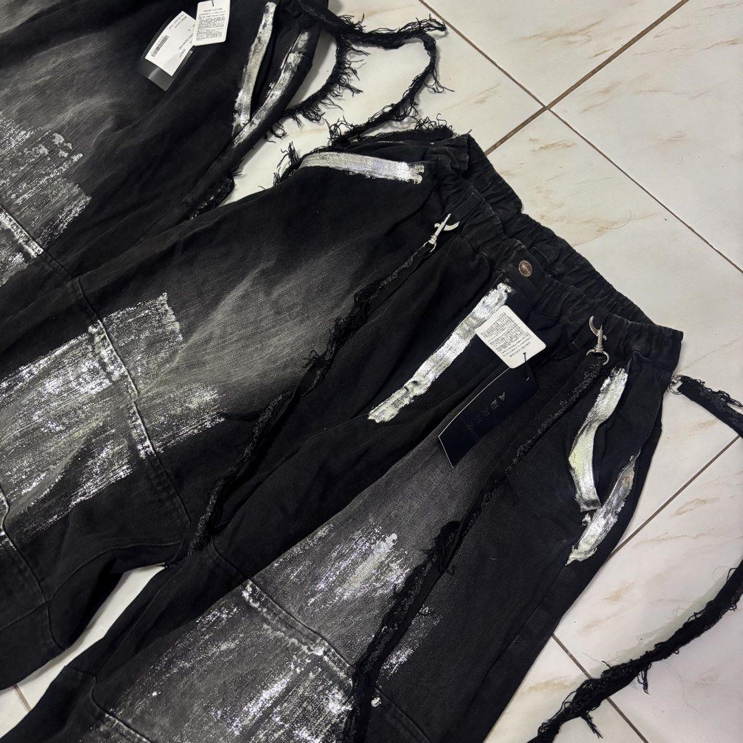 Adrer japanese pants (Category: Jeans) located in San Fernando. Submitted by diff.thr1ft (Listing ID 1468115366, Image 3). Description: - Brand: Adrer - Color: Black with silver metallic/foil distressed print details - Style: Japanese streetwear, wide-leg fit - Features: Elastic high waist, distressed raw edges, side straps with metal hardware, branded button - Condition: Brand new with tags (BNWT) - Perfect for daily casual wear or edgy streetwe