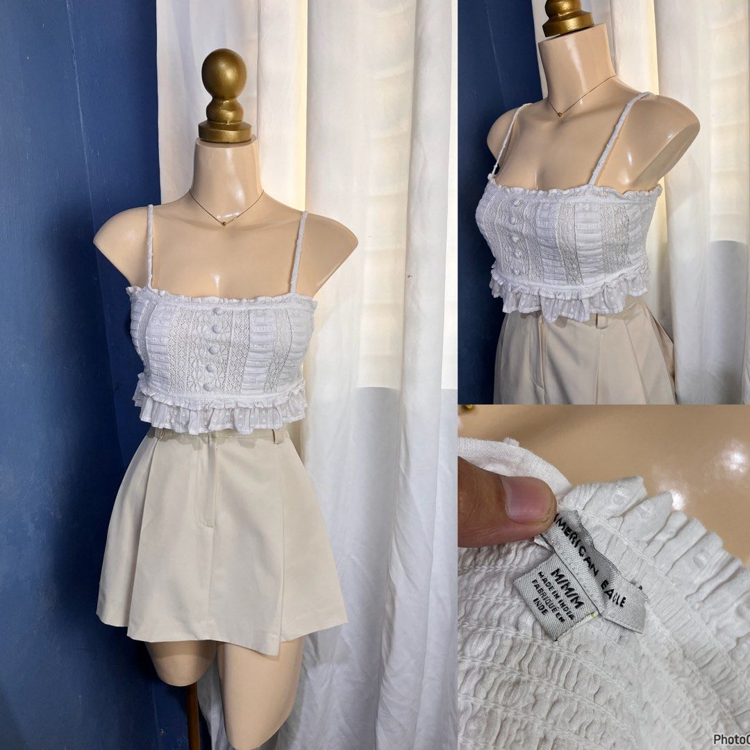American Eagle White Crop Top (Category: Shirts) located in Valencia. Submitted by kathrift (Listing ID 1468159413, Image 1). Description: - Brand: American Eagle - Size: M - Color: White - Details: Spaghetti straps, square neckline with ruffle trim, decorative front buttons, textured dot pattern, and a shirred smocked back panel - Origin: Made in India - Styling: Great to pair with high-waisted shorts or skirts.