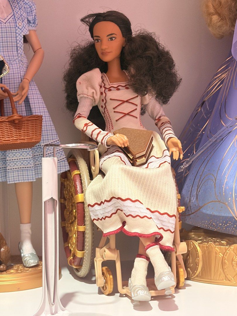 BARBIE WICKED NESSA (Category: Kids Toys) located in Caloocan City. Submitted by mgabbisaniel (Listing ID 1468230099, Image 1). Description: - Type: Collector doll in a decorated wheelchair - Appearance: Dark curly hair, brown eyes - Outfit: Cream-colored dress with red stitching, puff sleeves, white socks, and silver shoes - Accessories: Holding a small brown book - Condition: Clean, well-maintained display piece.