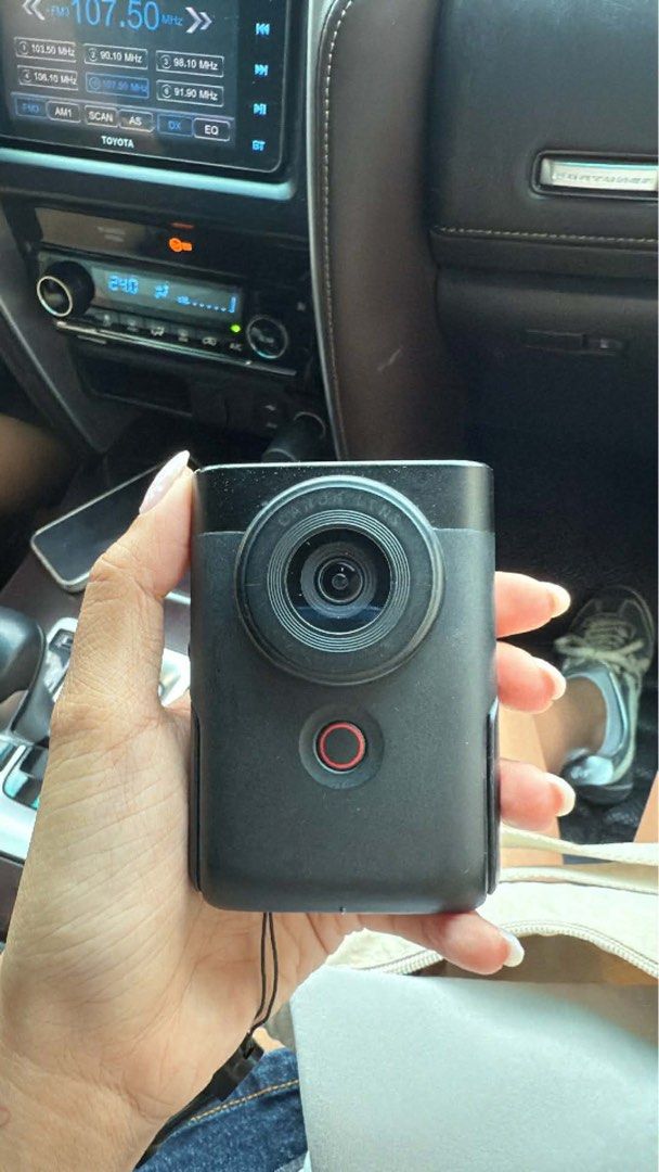 Canon V10 (Category: Cameras) located in Manila. Submitted by migsantos57184 (Listing ID 1468097602, Image 1). Description: - Color: Sleek black body with a stylish red circle accent - Design: Compact and ergonomic shape, easy to hold in one hand - Lens: Round lens barrel on the front - Portability: Includes a black wrist strap attached at the bottom corner for extra security - Condition: Ready to use for your daily photography needs.