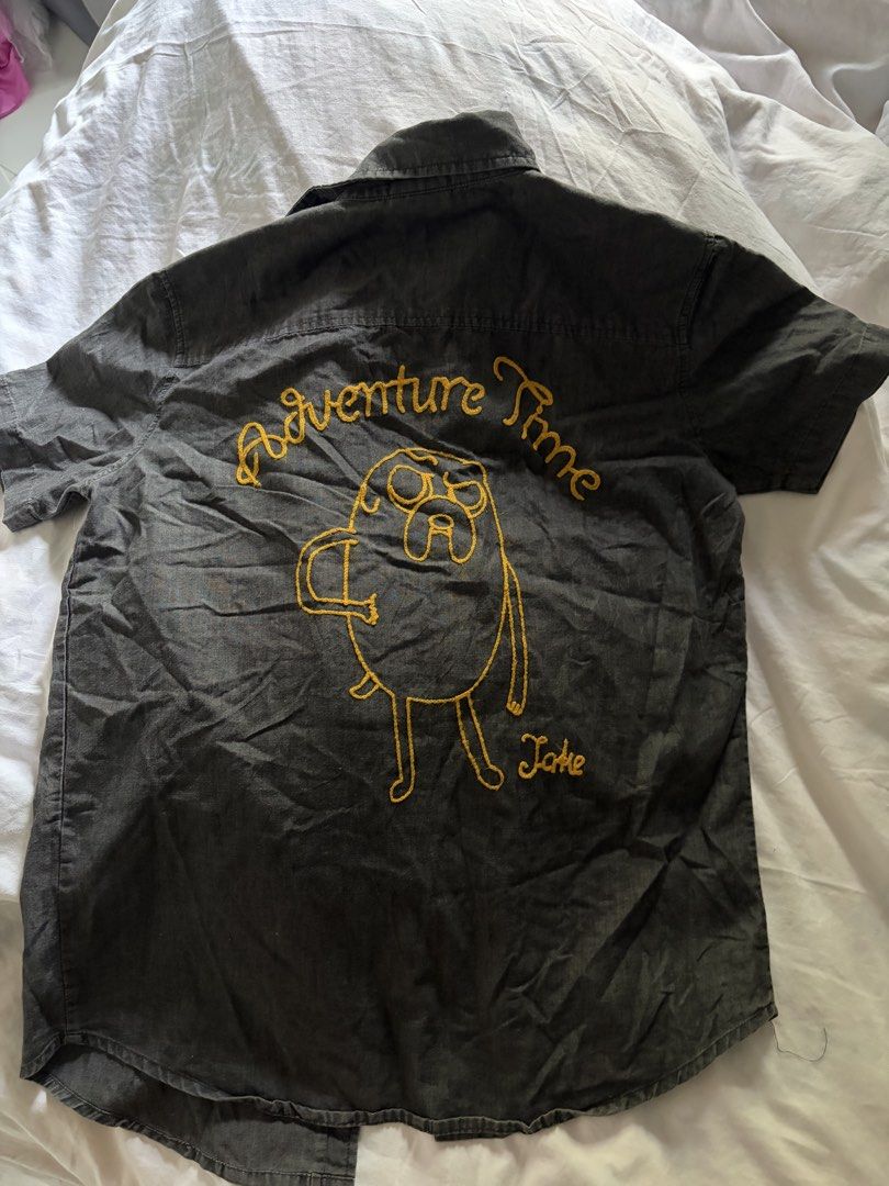 Cartoon Network Adventure Time Jake button-down shirt (Category: Tshirts & Polo Shirts ) located in General Santos City (Dadiangas). Submitted by jwtfg (Listing ID 1468112074, Image 1). Description: - Official Cartoon Network Adventure Time merchandise - Color: Dark grey short-sleeve button-down shirt - Back details: Embroidered Adventure Time text and Jake graphic - Front details: Dual chest pockets with embroidered logo and yellow Jake patch .