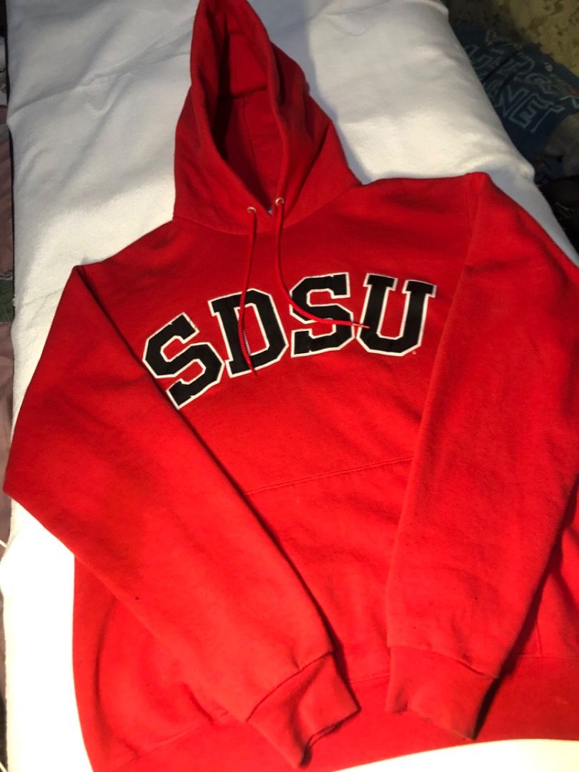 Champion SDSU Red Collegiate Hoodie (Category: Hoodies) located in Cavite. Submitted by puredolphin.2b4cb1 (Listing ID 1468143537, Image 2). Description: - Brand: Champion - Style: Hoodie with front pouch pocket and drawstring hood - Design: SDSU collegiate lettering across the chest - Color: Red - Size: Medium (M) - Material: 50% cotton, 50% polyester blend - Origin: Made in El Salvador.