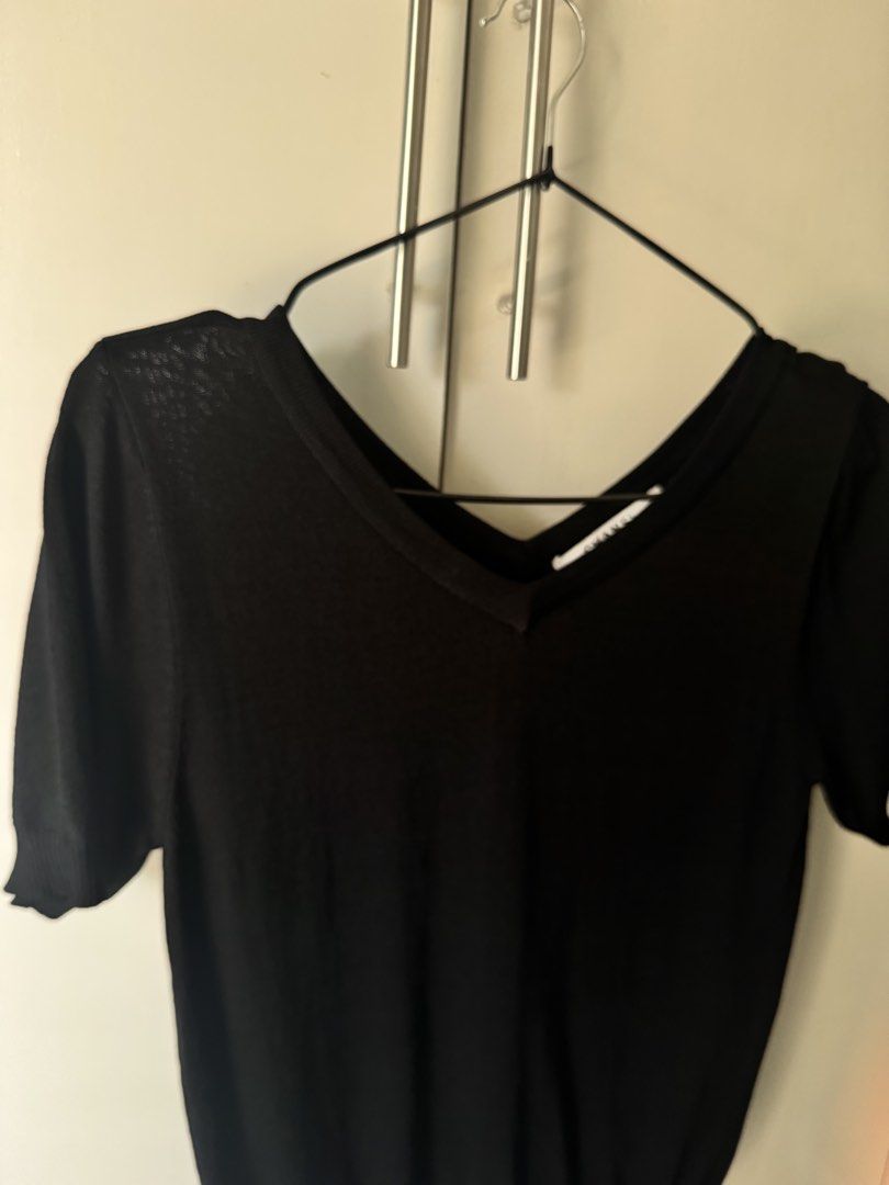 Chanel Black V-Neck Knit Top (Category: Blouses) located in Rosales. Submitted by thriftingismygame (Listing ID 1468178849, Image 2). Description: - Brand: Chanel - Style: Short-sleeve knit top with V-neck - Color: Classic Black - Details: Ribbed cuffs and hem, small decorative metallic logo badge near the bottom - Fabric: Lightweight with a slightly sheer texture - Condition: Clean overall, minimal wear - Perfect for: Elevating your everyday cas