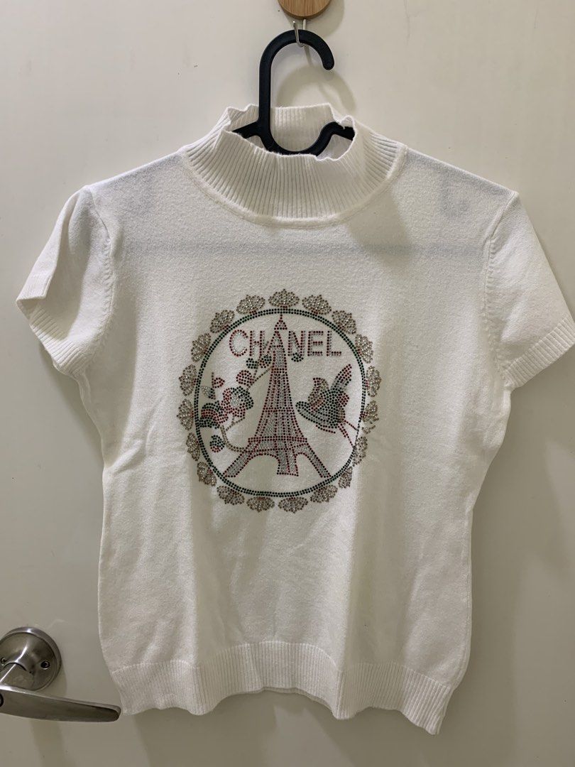Chanel White Short Sleeve Rhinestone Eiffel Tower Sweater (Category: Shirts) located in Manila. Submitted by jo.arban (Listing ID 1468224194, Image 1). Description: - Color: White - Style: Short sleeve knit sweater with mock neck - Design: Detailed rhinestone graphic featuring the Eiffel Tower, floral motifs, and Chanel lettering - Finishes: Ribbed collar, cuffs, and hem for a snug fit - Branding: Authentic black Chanel label inside the neckline 