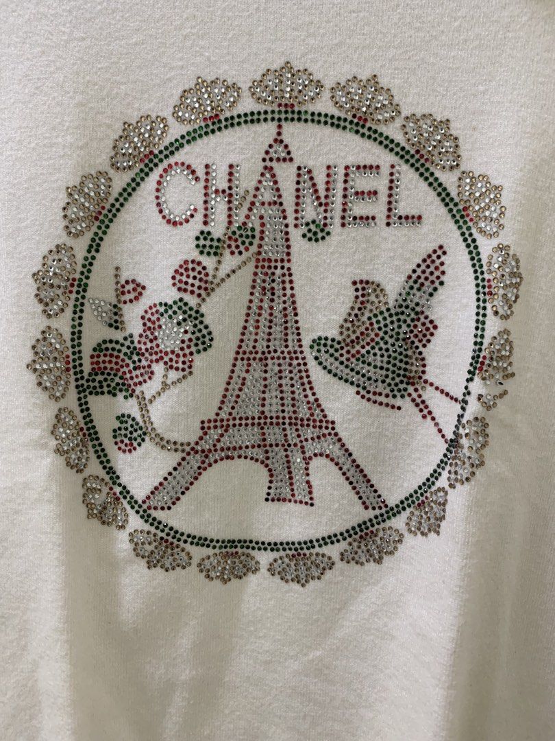 Chanel White Short Sleeve Rhinestone Eiffel Tower Sweater (Category: Shirts) located in Manila. Submitted by jo.arban (Listing ID 1468224194, Image 2). Description: - Color: White - Style: Short sleeve knit sweater with mock neck - Design: Detailed rhinestone graphic featuring the Eiffel Tower, floral motifs, and Chanel lettering - Finishes: Ribbed collar, cuffs, and hem for a snug fit - Branding: Authentic black Chanel label inside the neckline 