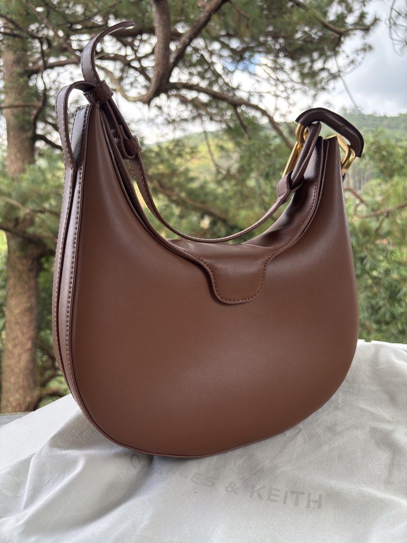 Charles & Keith Kora Metallic-Accent Moon Bag (Category: Shoulder Bags) located in Baguio. Submitted by thecuratedcartbymj (Listing ID 1468252015, Image 2). Description: Authentic Charles & Keith Kora Metallic-Accent Moon Bag Color: Brown Condition: Brand New / Unused (With original dust bag) ⚠️ PLEASE READ BEFORE BUYING (REASON FOR DISCOUNT): This gorgeous moon bag is completely brand new and has never been used. The interior, base, and main cre