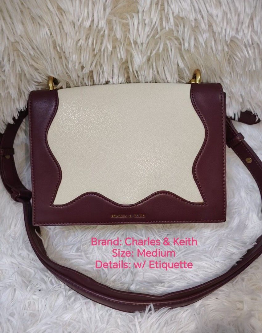 Charles & Keith Medium Two-Tone Crossbody Bag (Category: Cross-body Bags) located in Quezon City. Submitted by zhelcloset01 (Listing ID 1468069165, Image 1). Description: - Brand: Charles & Keith - Style: Medium shoulder bag with structured shape - Colorway: Two-tone cream and burgundy with elegant scalloped trim - Hardware: Gold-tone accents with engraved front branding - Strap: Includes a long adjustable shoulder strap - Closure: Flap closure w
